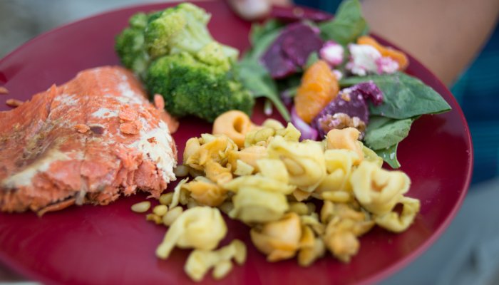 A red plate with salmon, broccoli, and tortellini