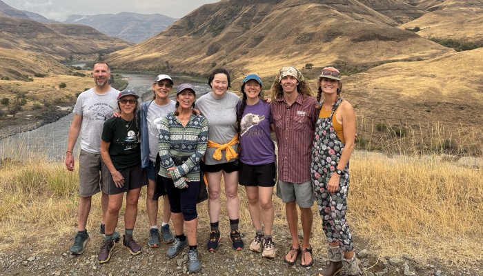 A group of ROW Adventures guides and guests standing on a hillside overlooking the Salmon River canyon, smiling after a day of rafting through Idaho’s rugged landscape.