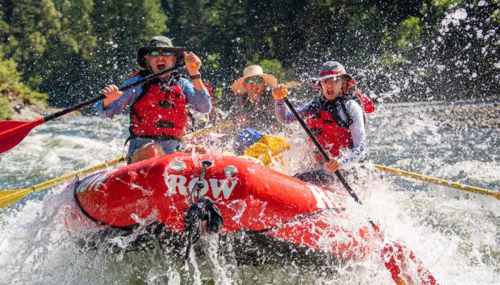 three people in red whitewater raft paddling