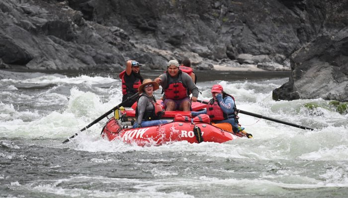 A group of young rafters from the Pandion Institute program navigate whitewater rapids in a red ROW raft, sharing smiles and celebration as they paddle downstream.